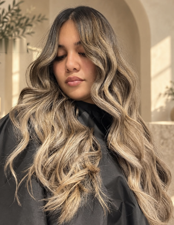Long bronde waves against a beige arched wall by Salon Maie